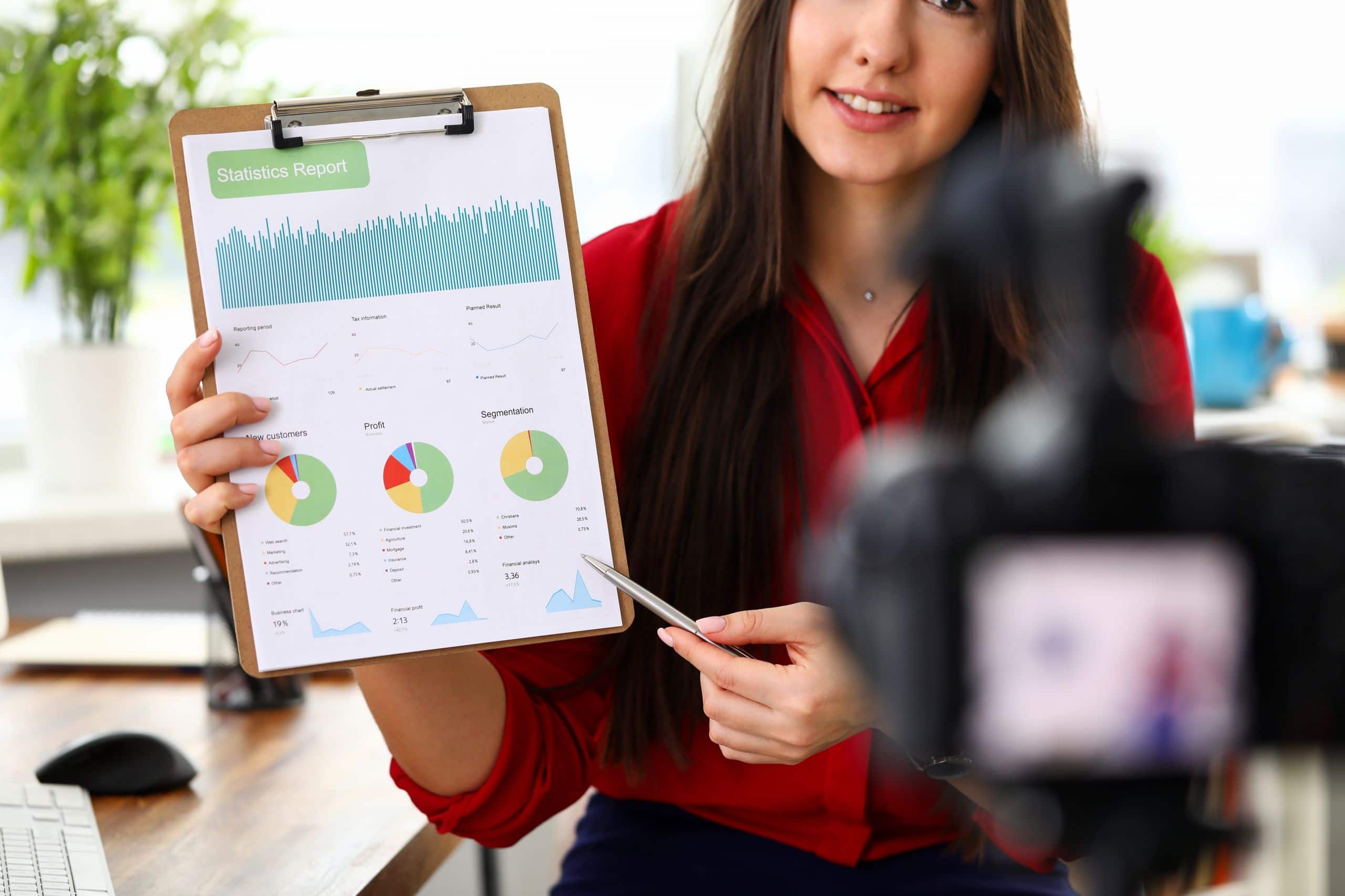Young woman sitting in office opposite camera and presenting statistics and analytics report.